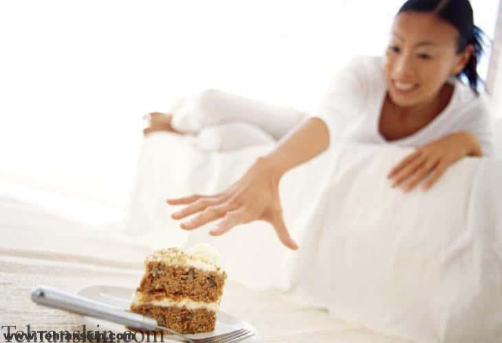 low angle view of a woman lying on a couch reaching for a slice of cake
