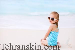 Little girl with bottle of sun cream sitting at tropical beach